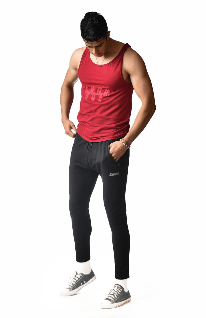 A man wearing black sweatpants and a red shirt stands confidently, showcasing a casual yet stylish outfit.