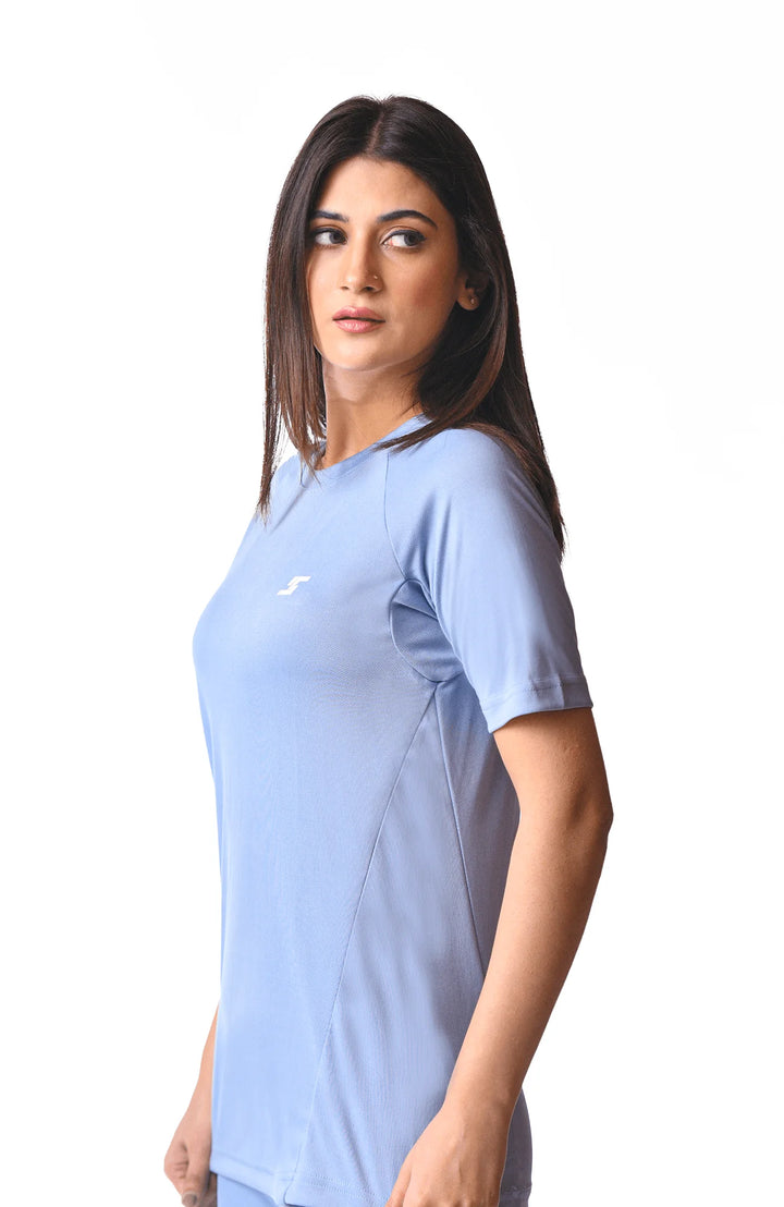 A woman dressed in a blue shirt and pants, standing confidently with a neutral background.