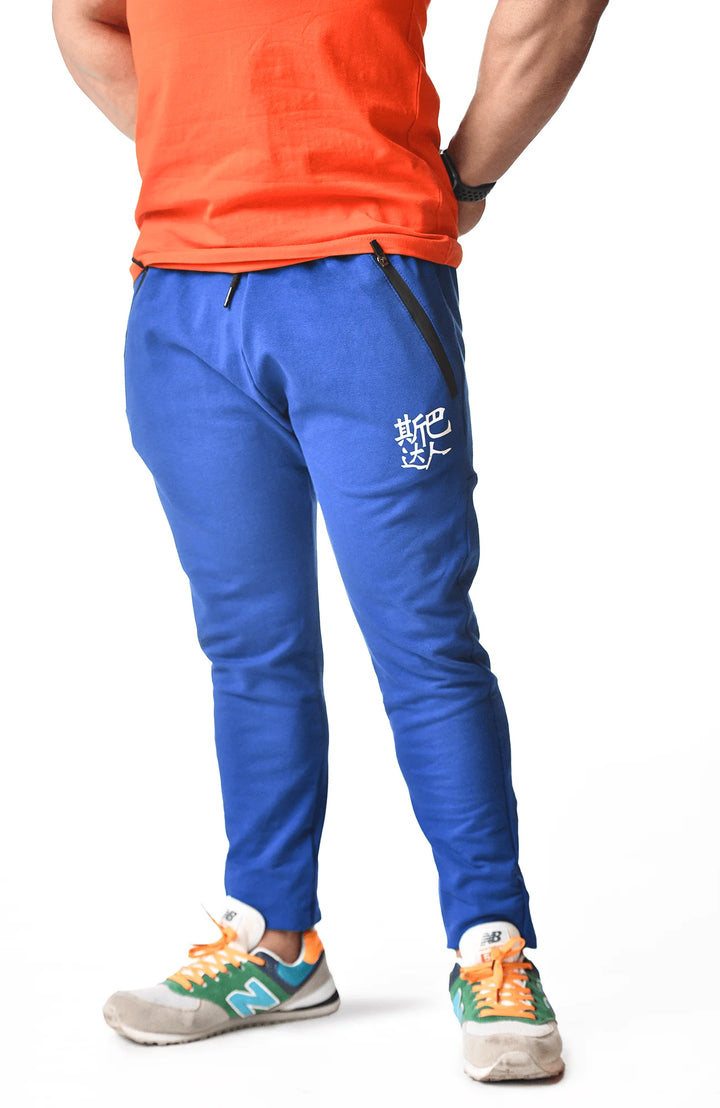 A man dressed in an orange shirt and blue sweatpants stands confidently, showcasing a casual and vibrant outfit.