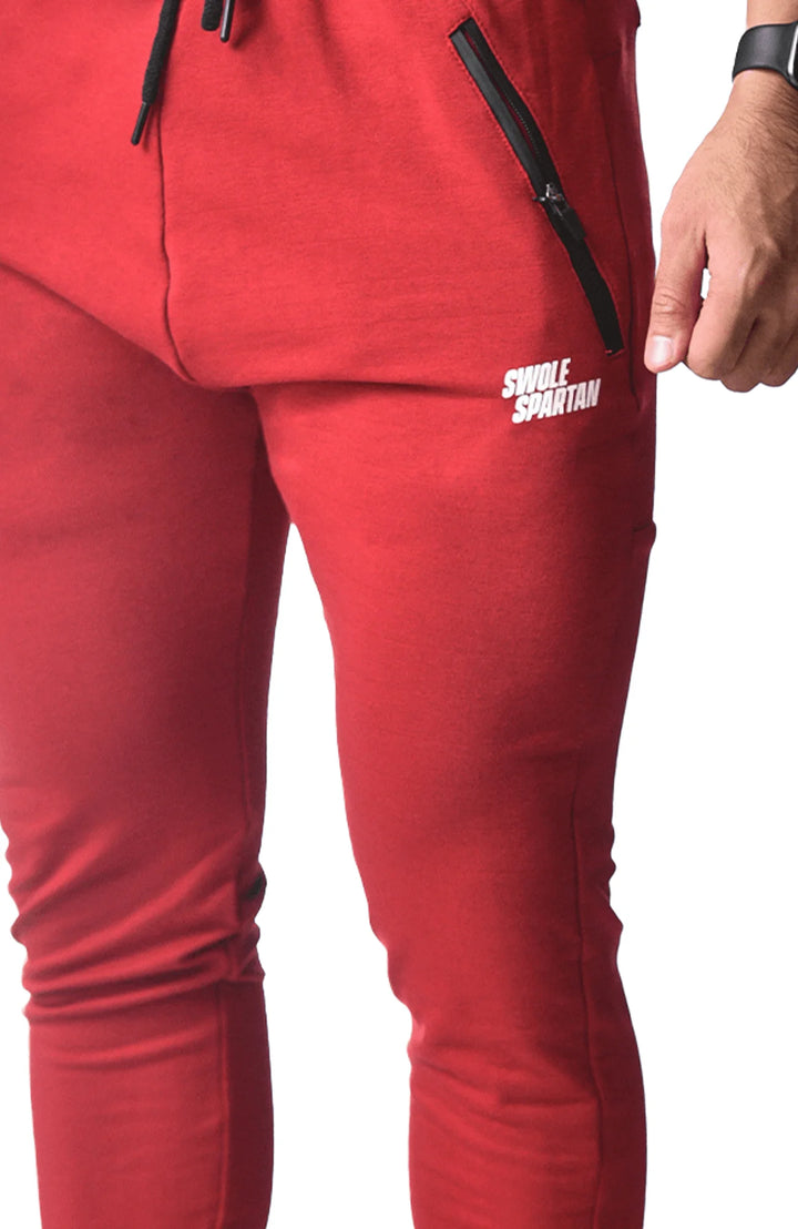  A man dressed in red sweatpants and white sneakers stands confidently, showcasing a casual and sporty style.