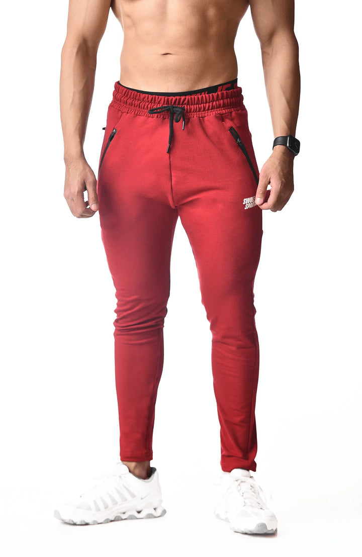  A man dressed in red sweatpants and white sneakers stands confidently, showcasing a casual and sporty style.